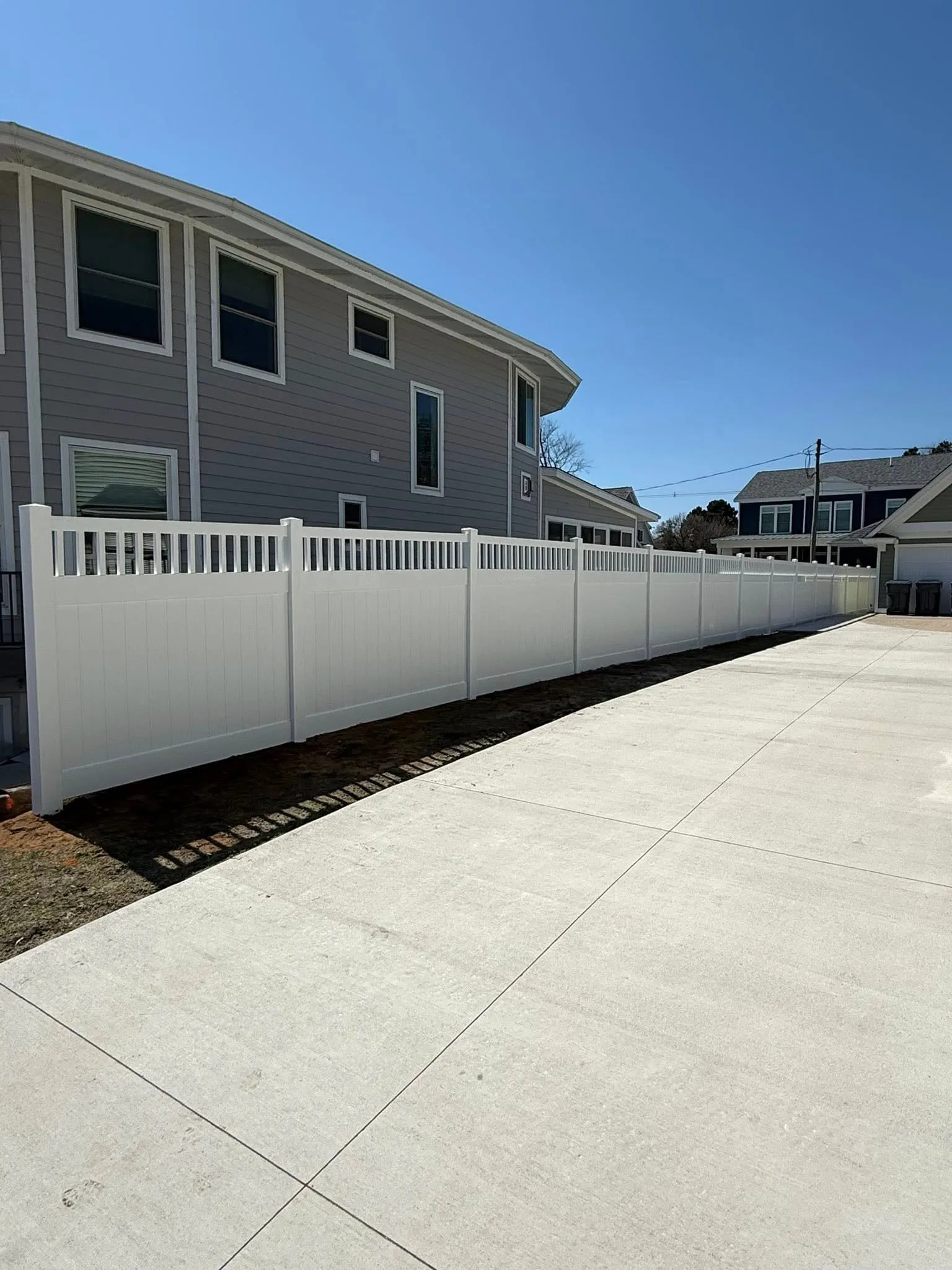 White vinyl privacy fence run along a driveway with a clean, consistent line and finished posts.