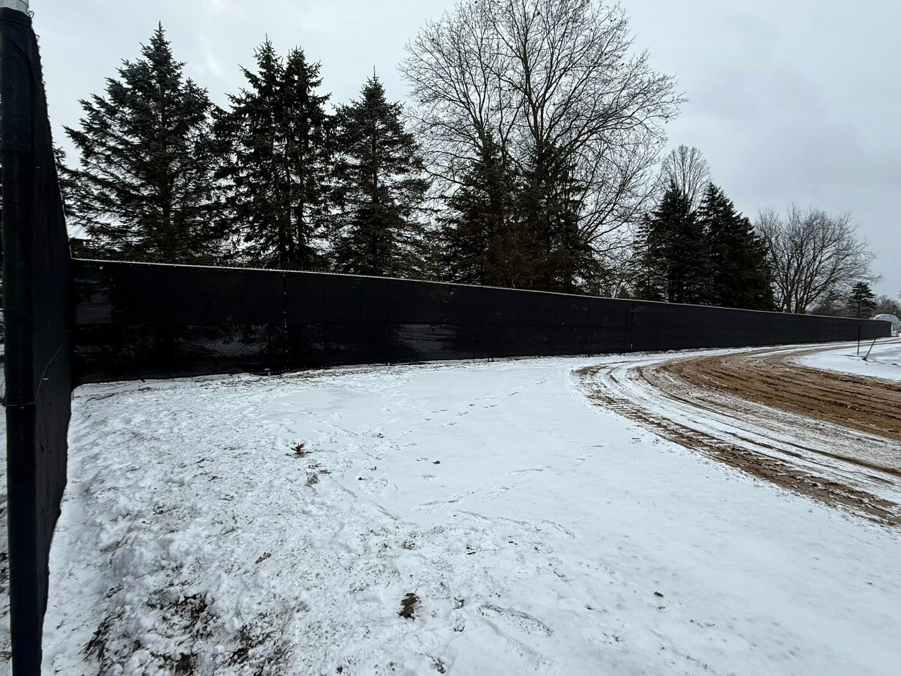Long privacy screen fence line in winter, installed for perimeter control along a work area.