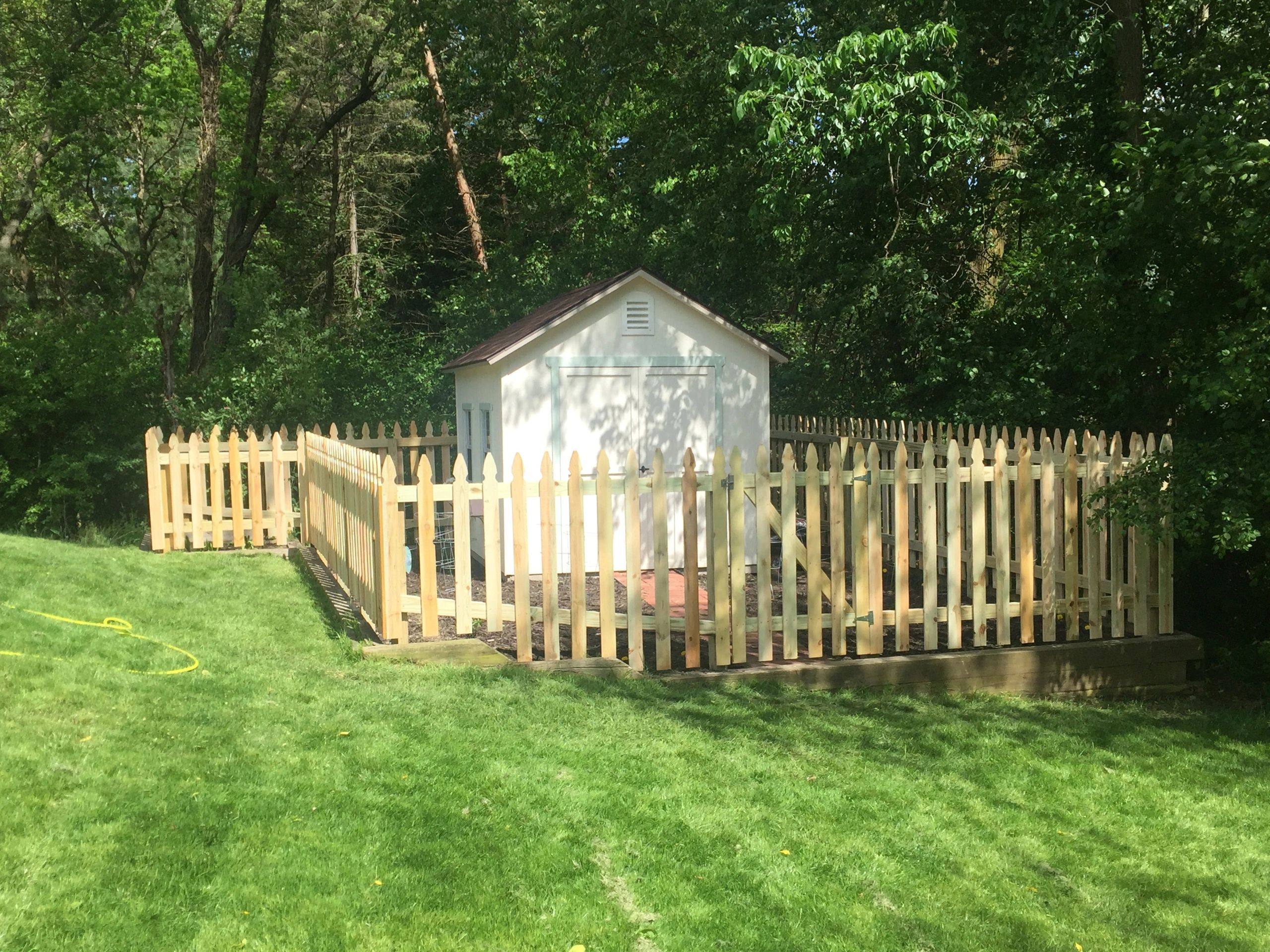 Picket enclosure fence around a backyard shed with a corner gate and clean layout lines.